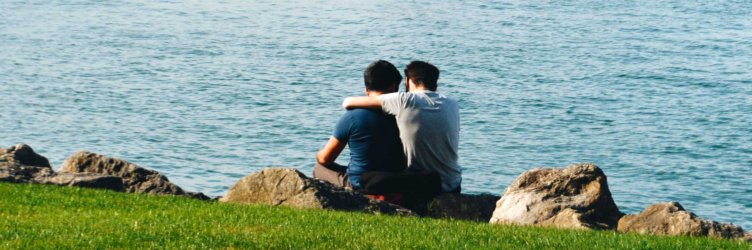 Two men hug by a body of water